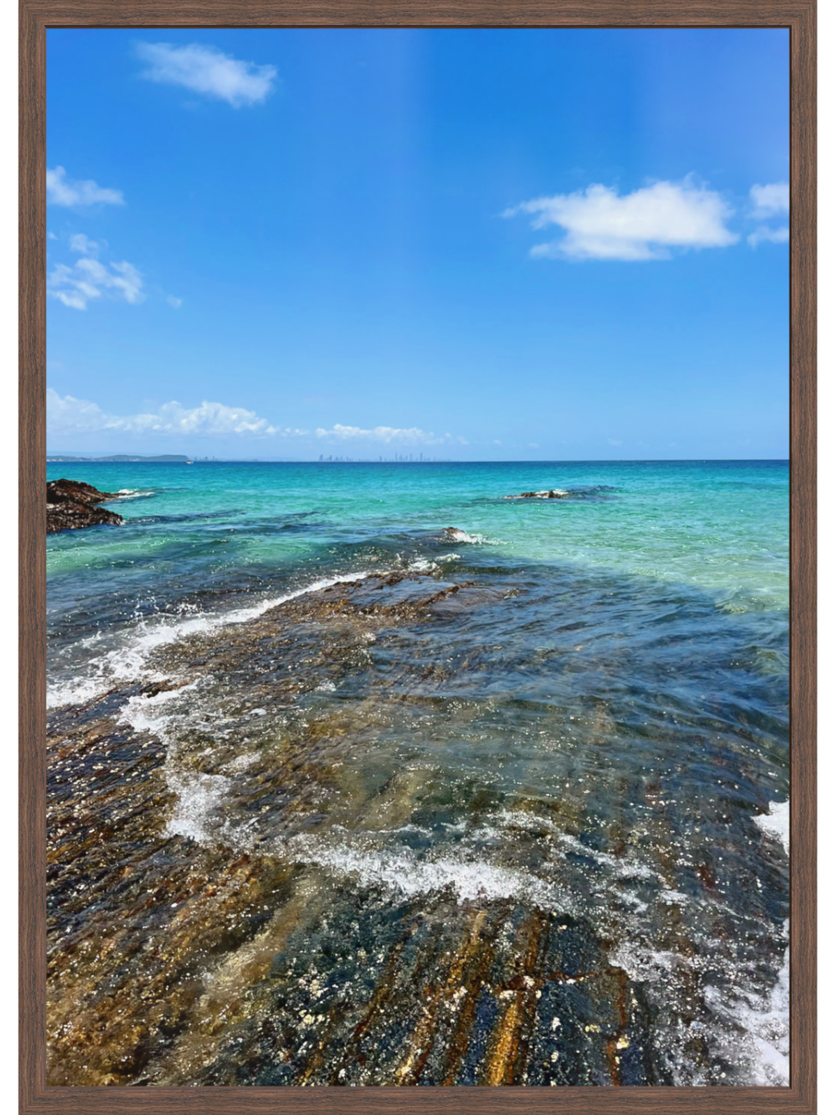 Coastal scene with clear blue water and rocky shoreline, framed in brown.