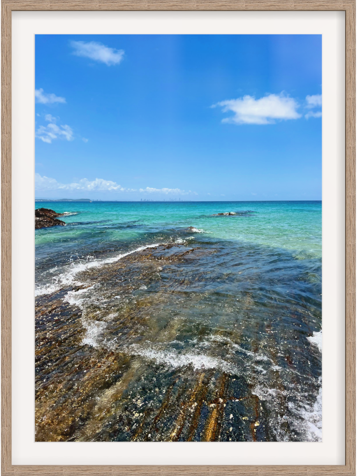 Framed photograph of a rocky shoreline with clear blue water and sky.