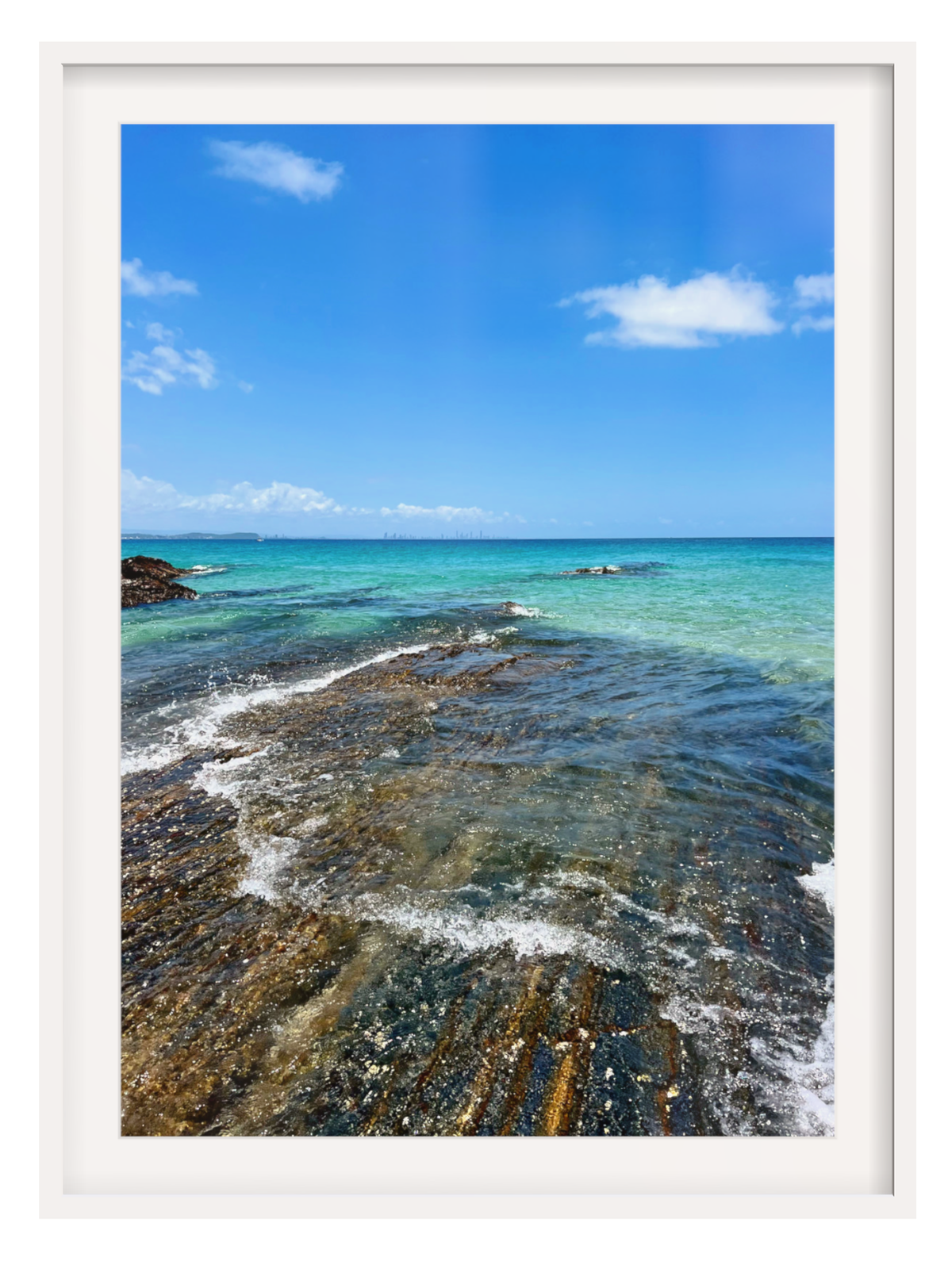 Coastal scene with clear blue water and rocky shoreline, framed in white.