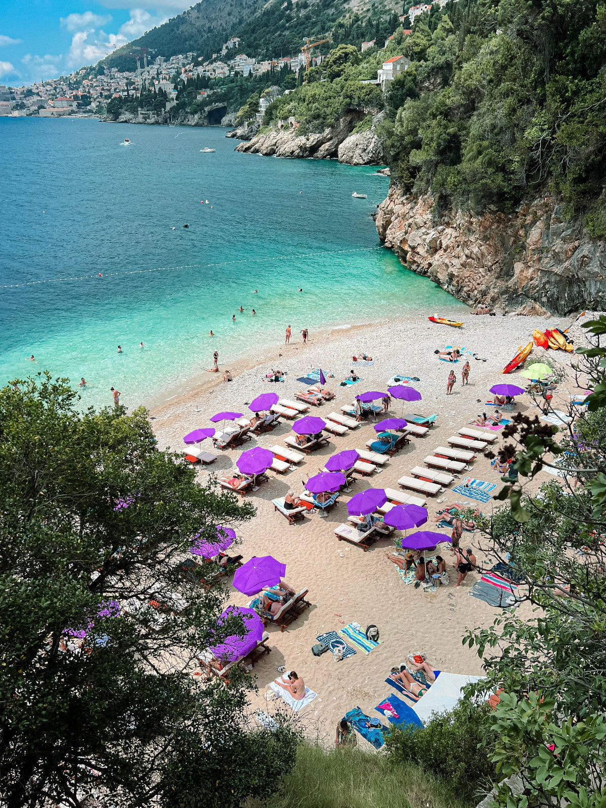 Beach scene with purple umbrellas and people enjoying the sun on a sandy shore.