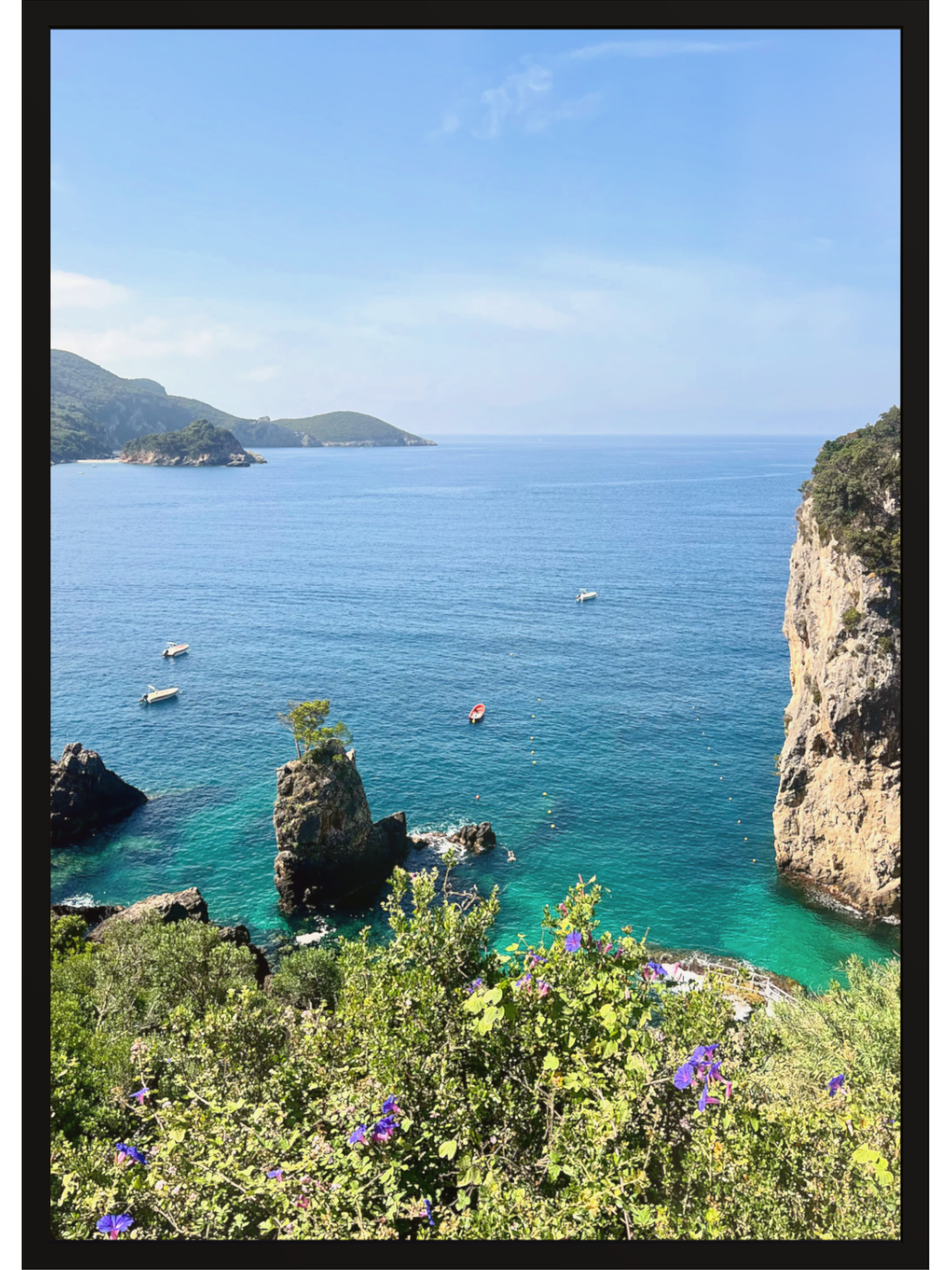 Coastal scene with clear blue water, rocky cliffs, and boats near a mountainous island.
