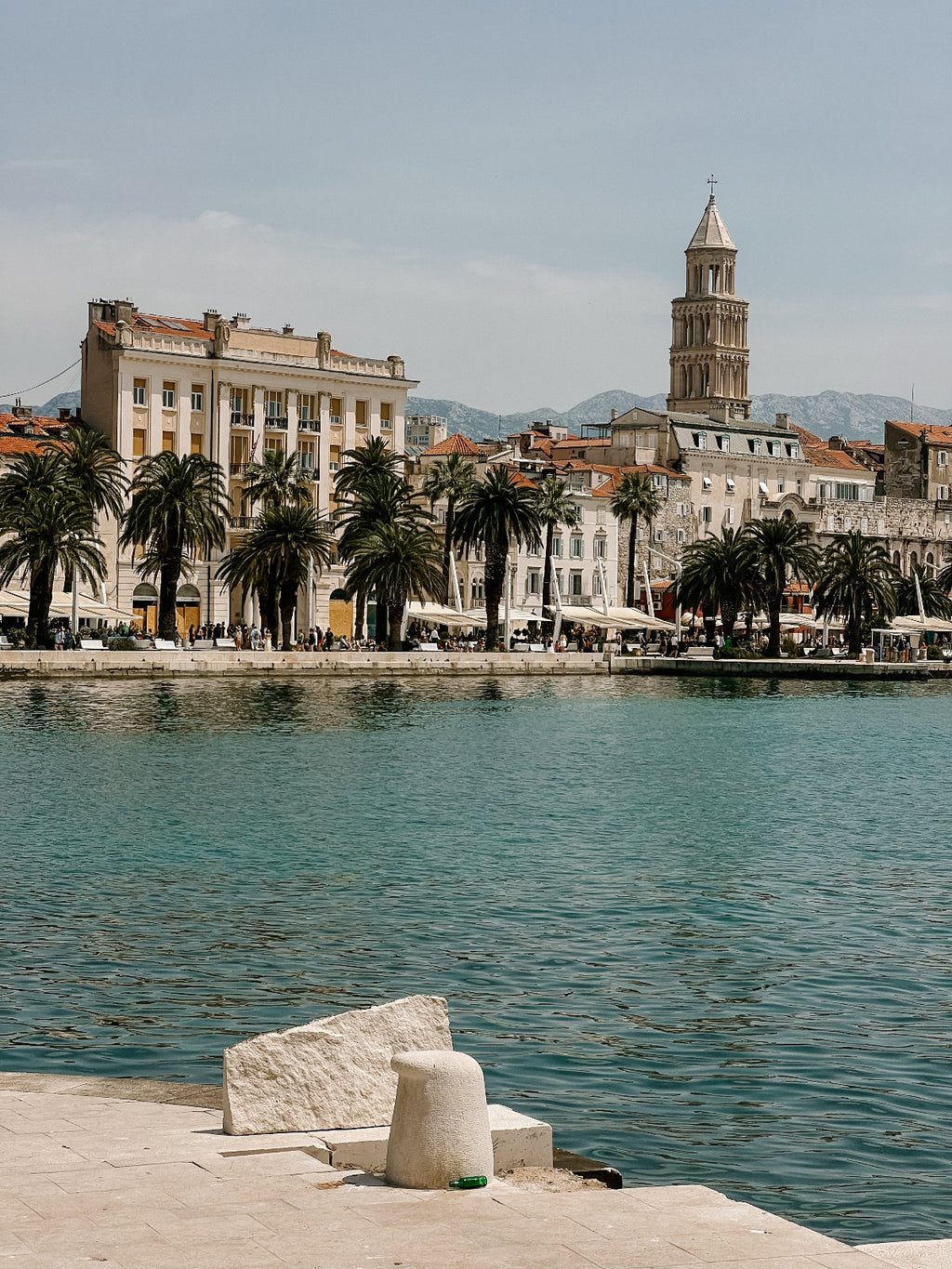 Cityscape with waterfront, palm trees, and a prominent tower.