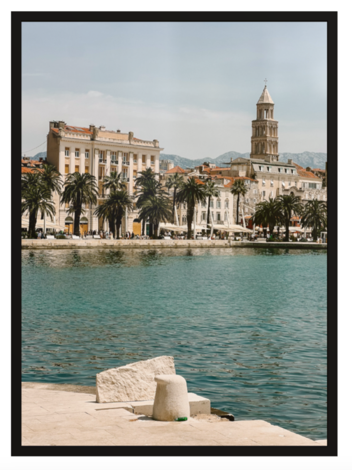 Cityscape with waterfront and historic buildings, including a tower, with palm trees lining the shore.