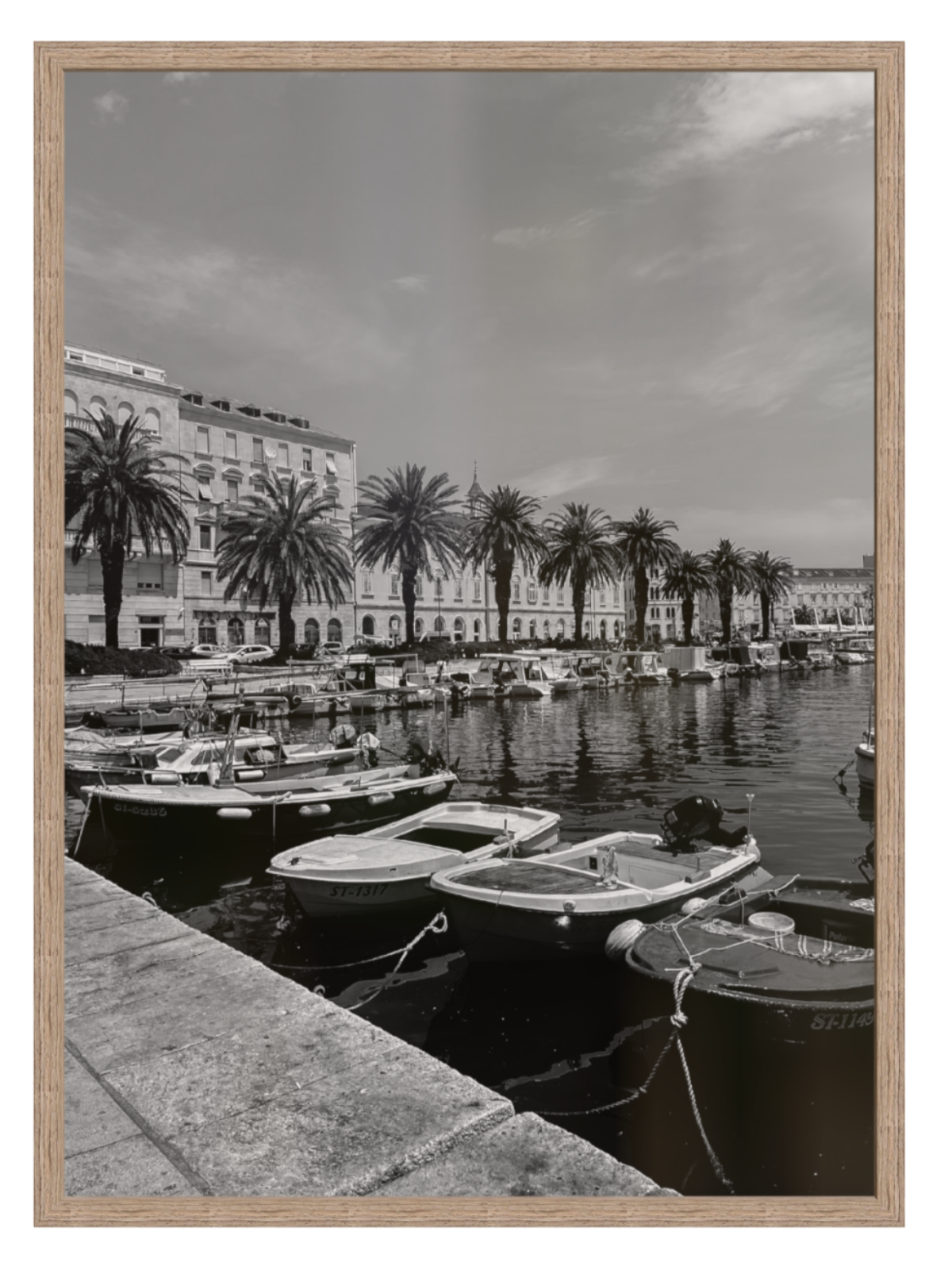 Black and white photograph of a harbor scene with boats and palm trees, framed in a light wood border.