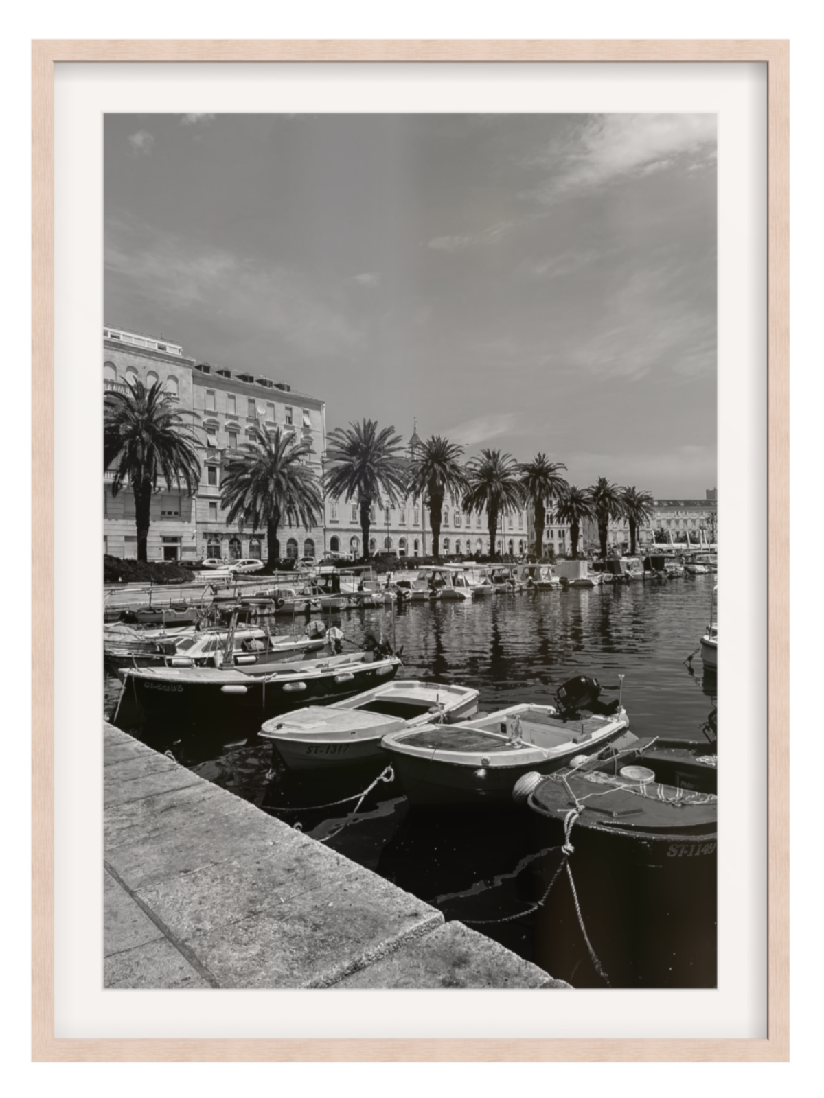 Black and white photograph of a harbor with boats and palm trees, framed in a light wood border.