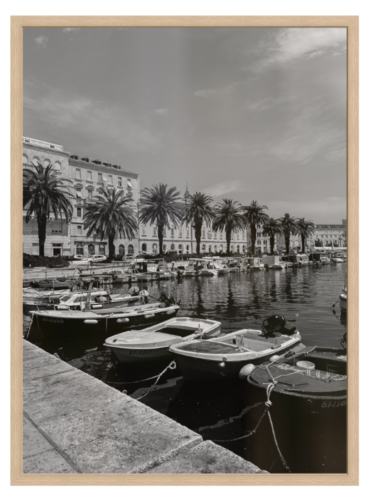 Harbor scene with boats and palm trees under a cloudy sky, framed in wood.