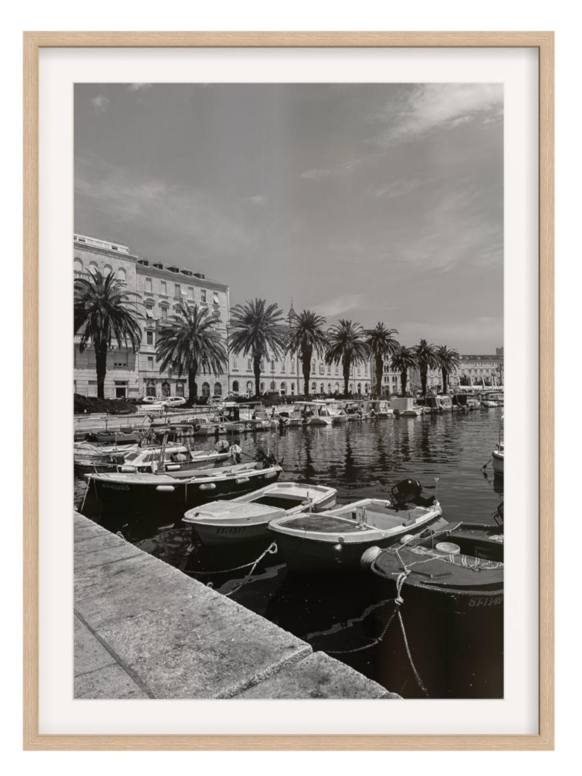 Black and white photograph of a harbor with boats and palm trees, framed in a light wood border.