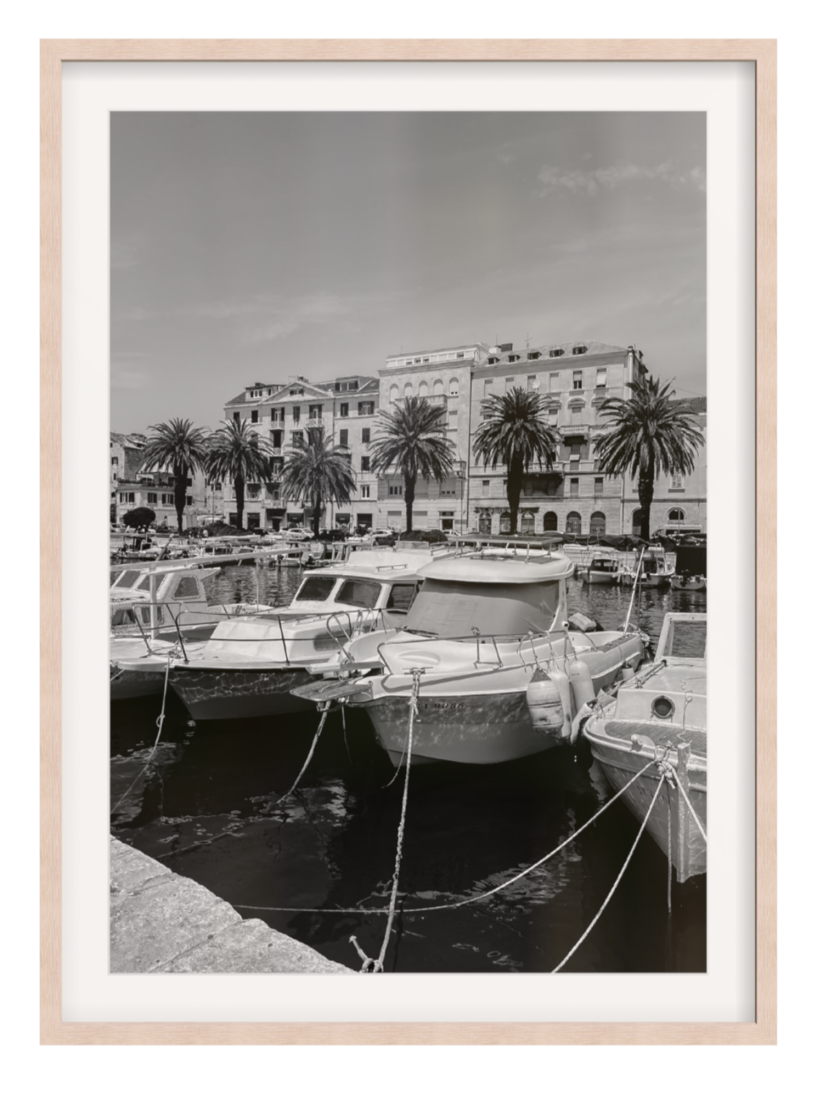 Harbor scene with boats and buildings, framed in a light wood frame.