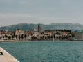 Cityscape with a prominent clock tower by a body of water, mountains in the background