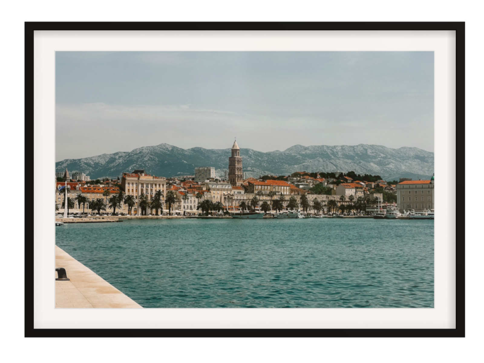 Cityscape with a clock tower and mountains in the background, framed picture.