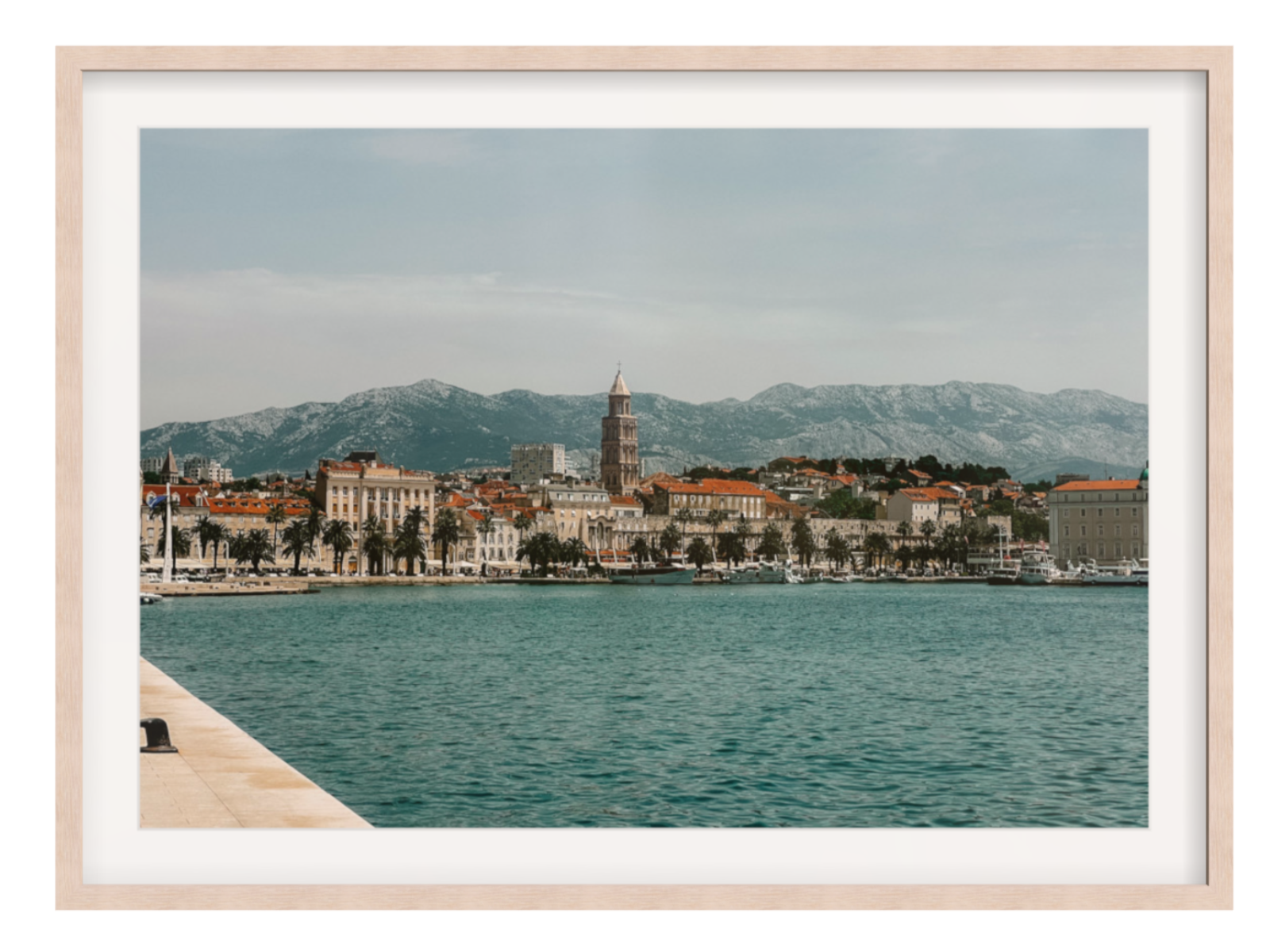 Framed photograph of a coastal city with mountains in the background. Split landscape light oak frame with border