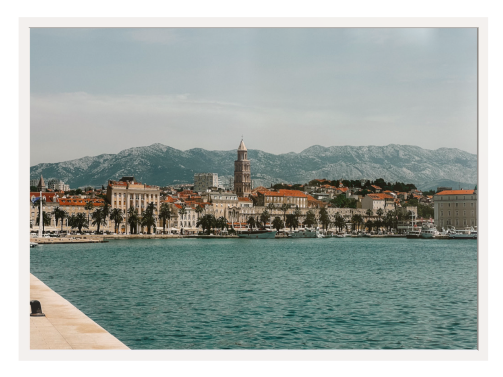 Cityscape with a clock tower by a body of water and mountains in the background. Split landscape white frame 