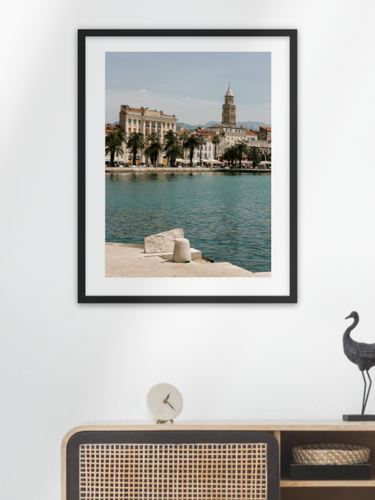 Framed photograph of a coastal cityscape on a wall above a wooden shelf with decorative items.