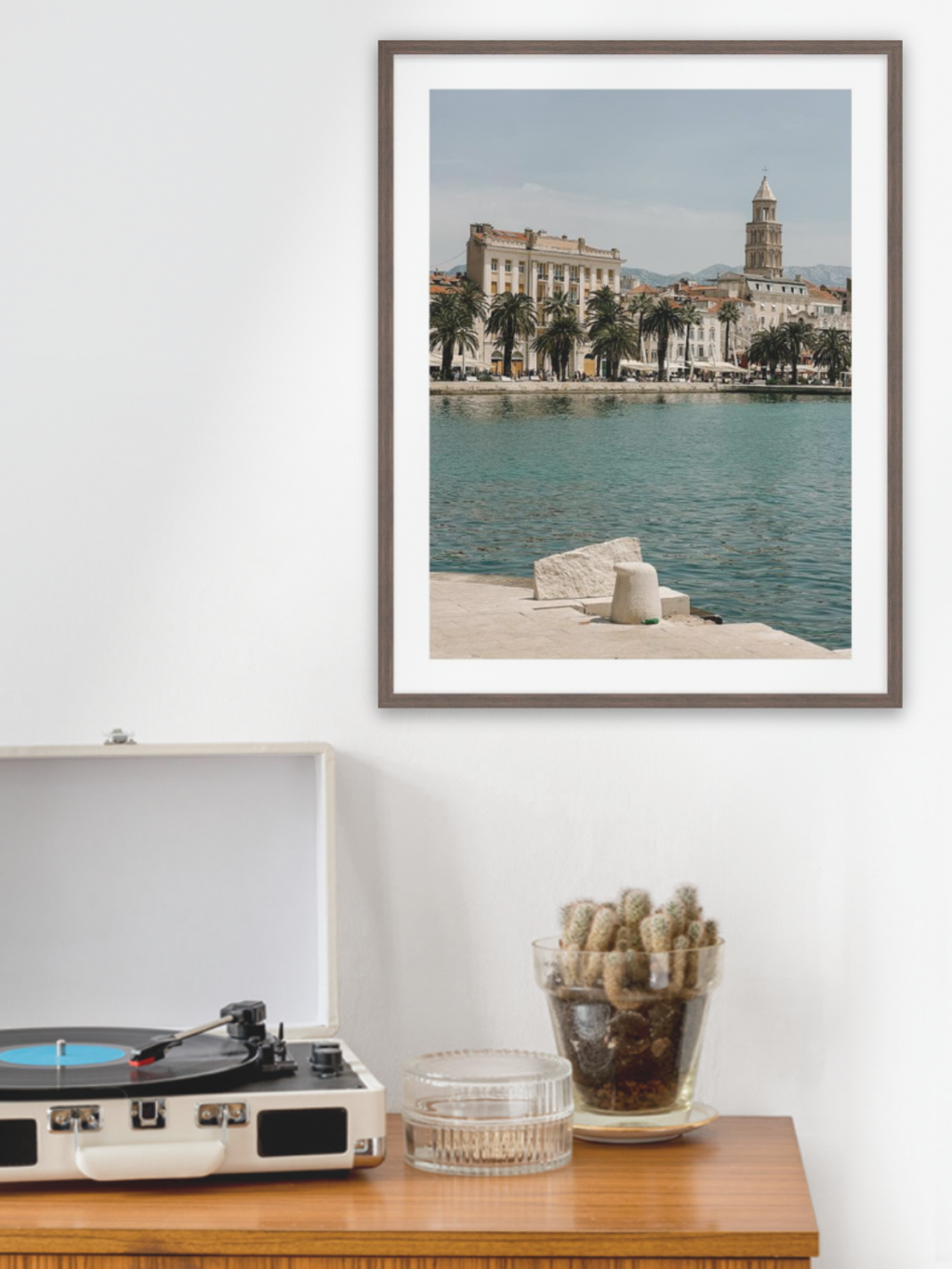 Framed photograph of a coastal scene above a record player on a wooden surface.