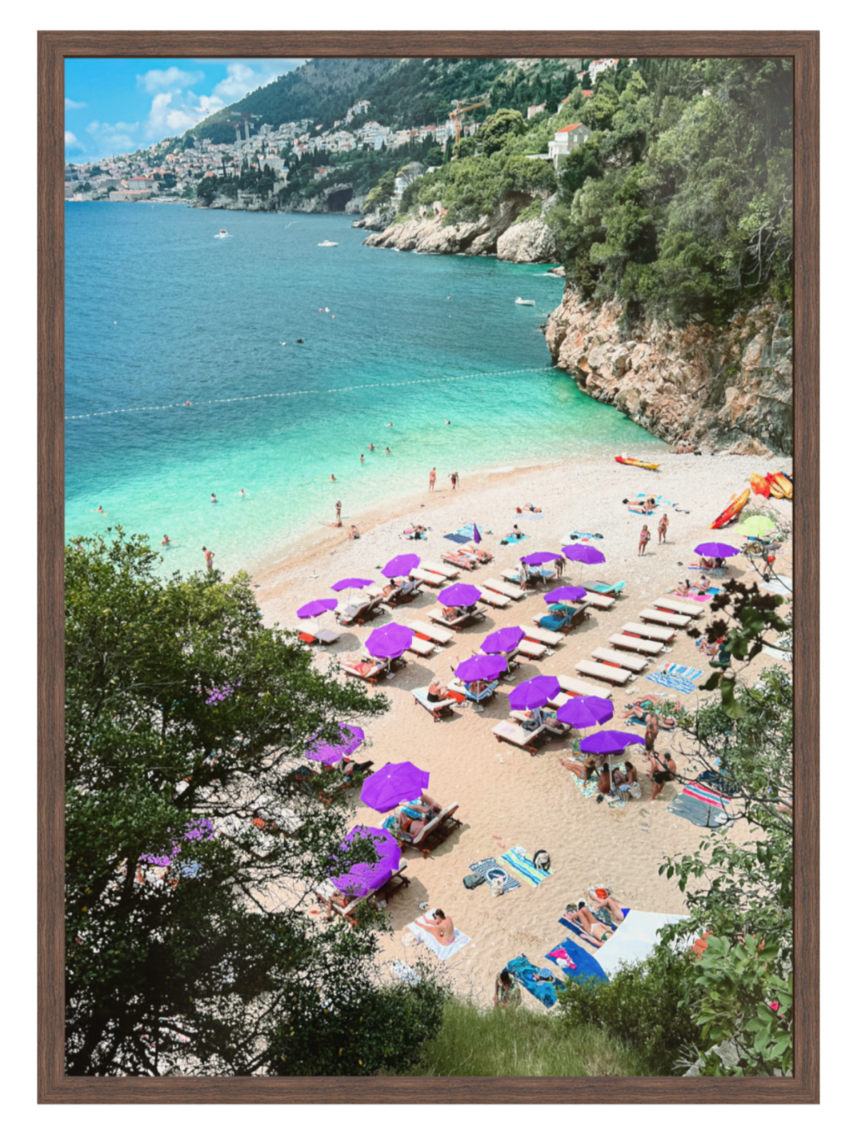 Beach scene with purple umbrellas and people, surrounded by greenery and a mountainous background.