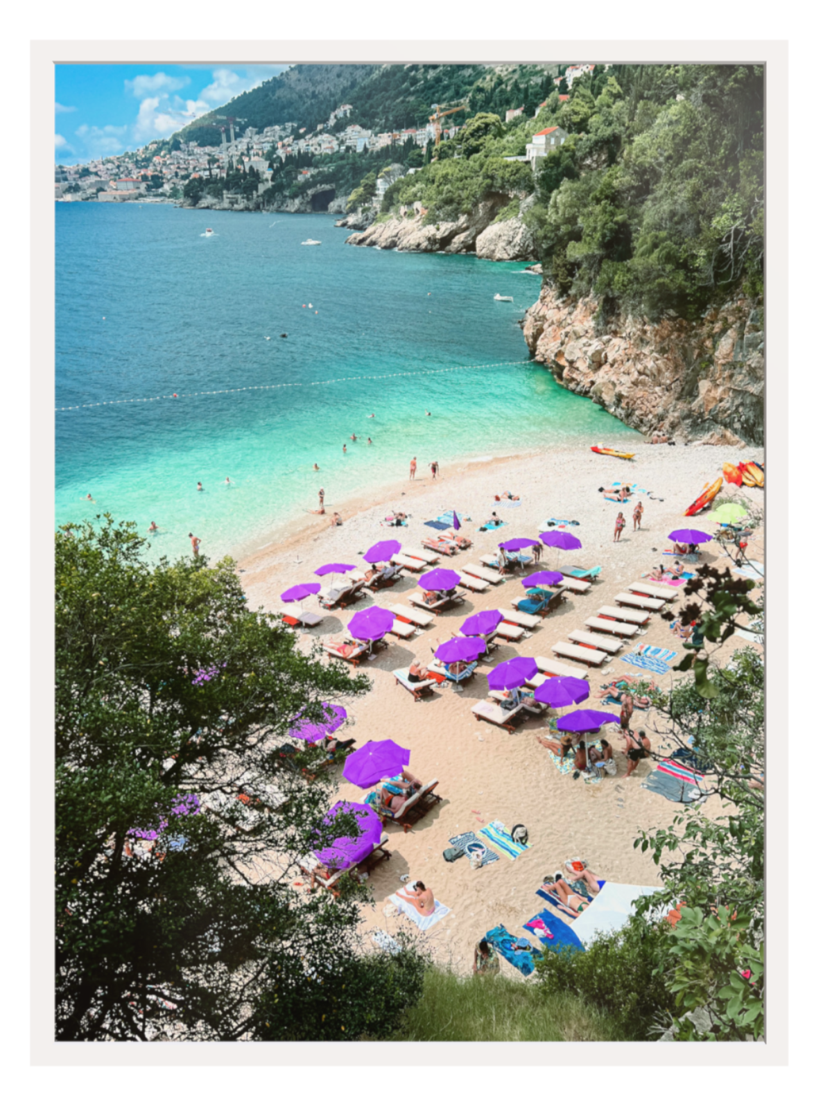 Beach scene with people under purple umbrellas and turquoise water.