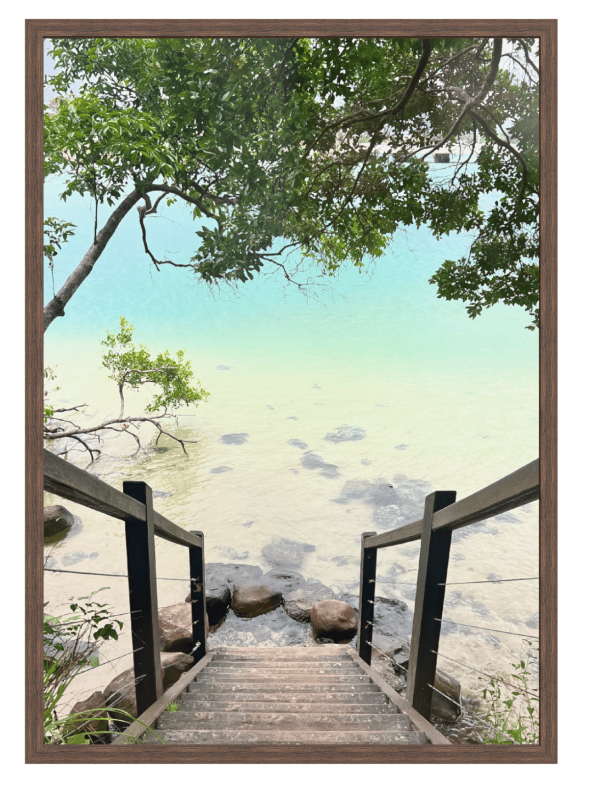 Wooden pathway leading to a serene beach scene with trees and rocks.