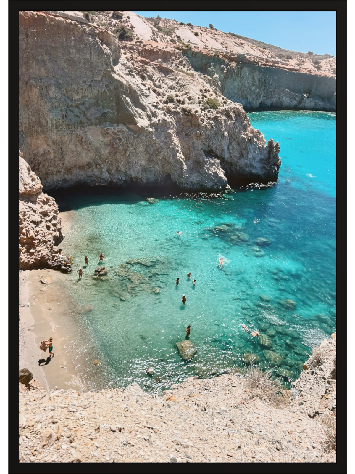Cove with clear blue water and rocky cliffs, people swimming and sunbathing.