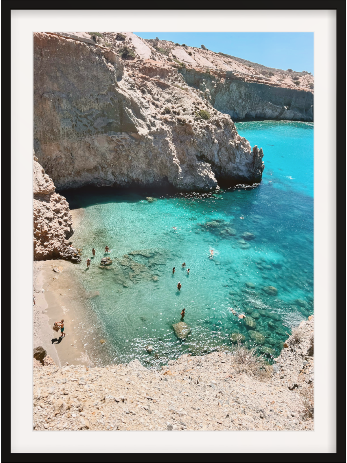 Turquoise cove with rocky cliffs and people swimming, framed as a print.