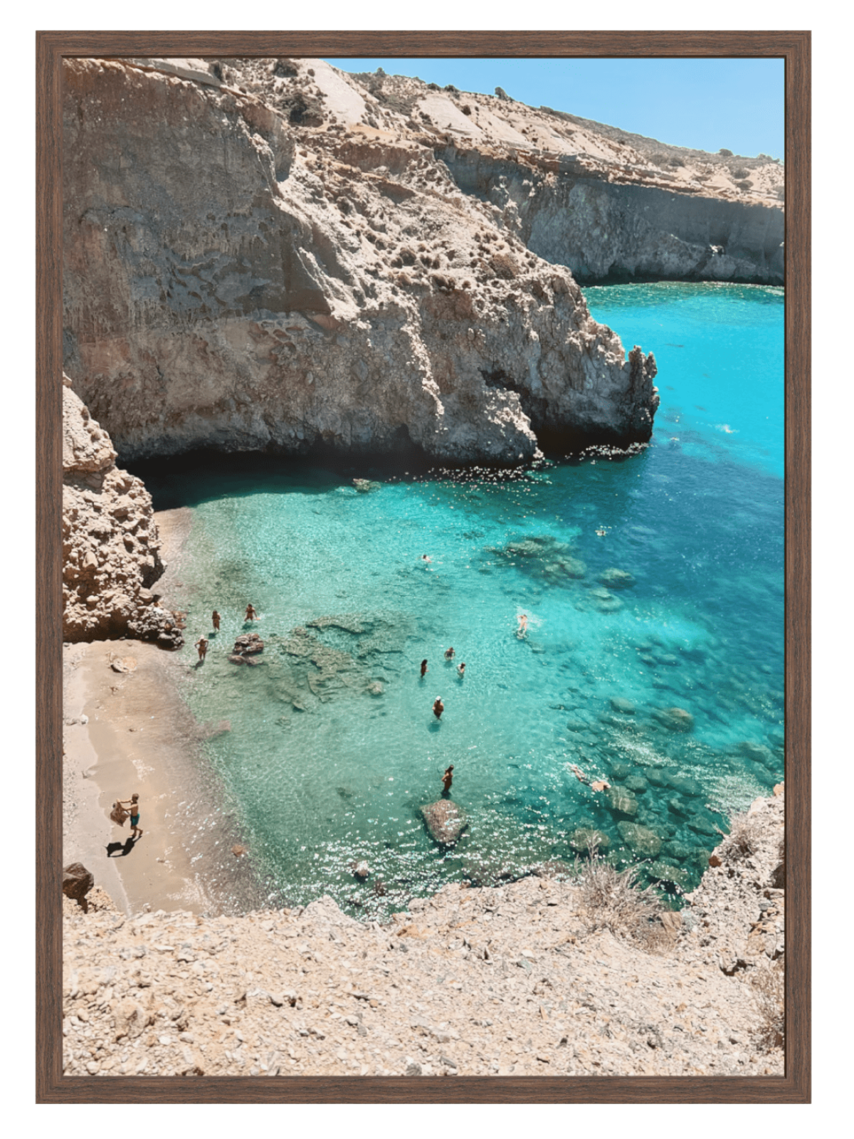 Cove with clear blue water and rocky cliffs, people swimming and sunbathing.