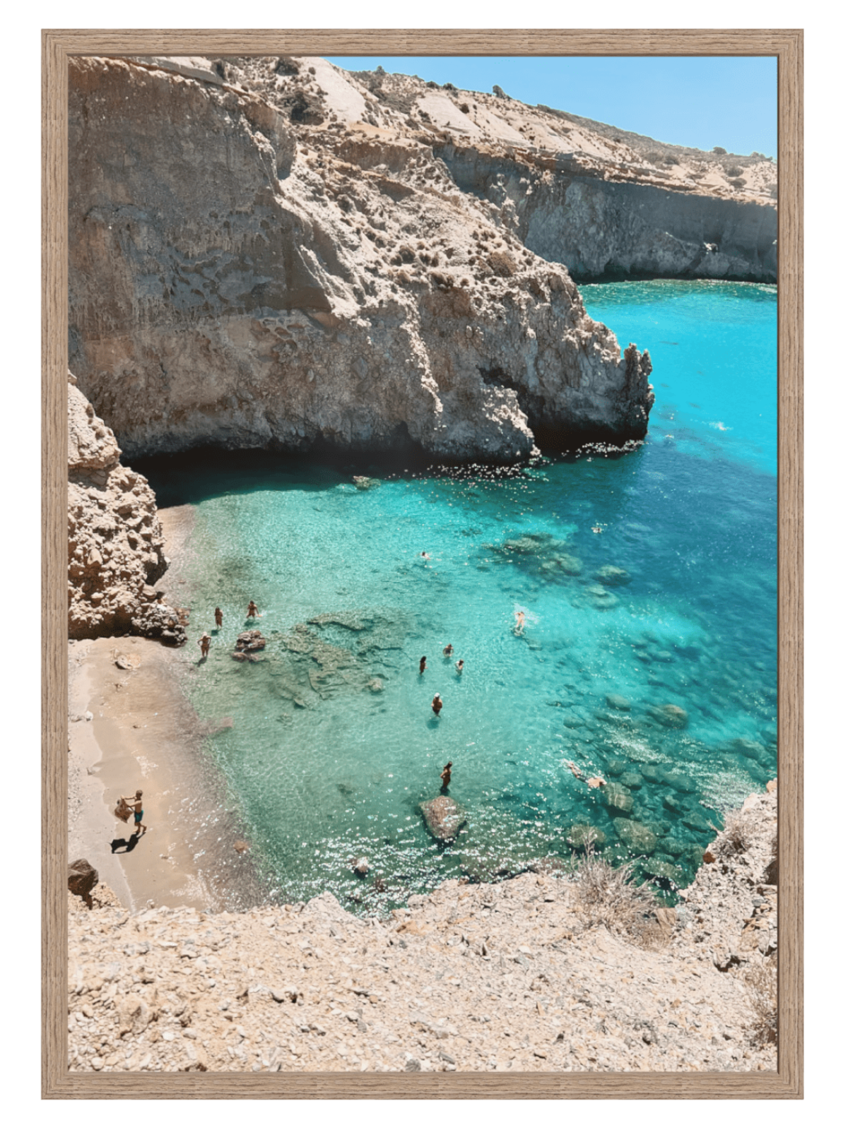 Beach scene with clear blue water and rocky cliffs, framed as a picture.