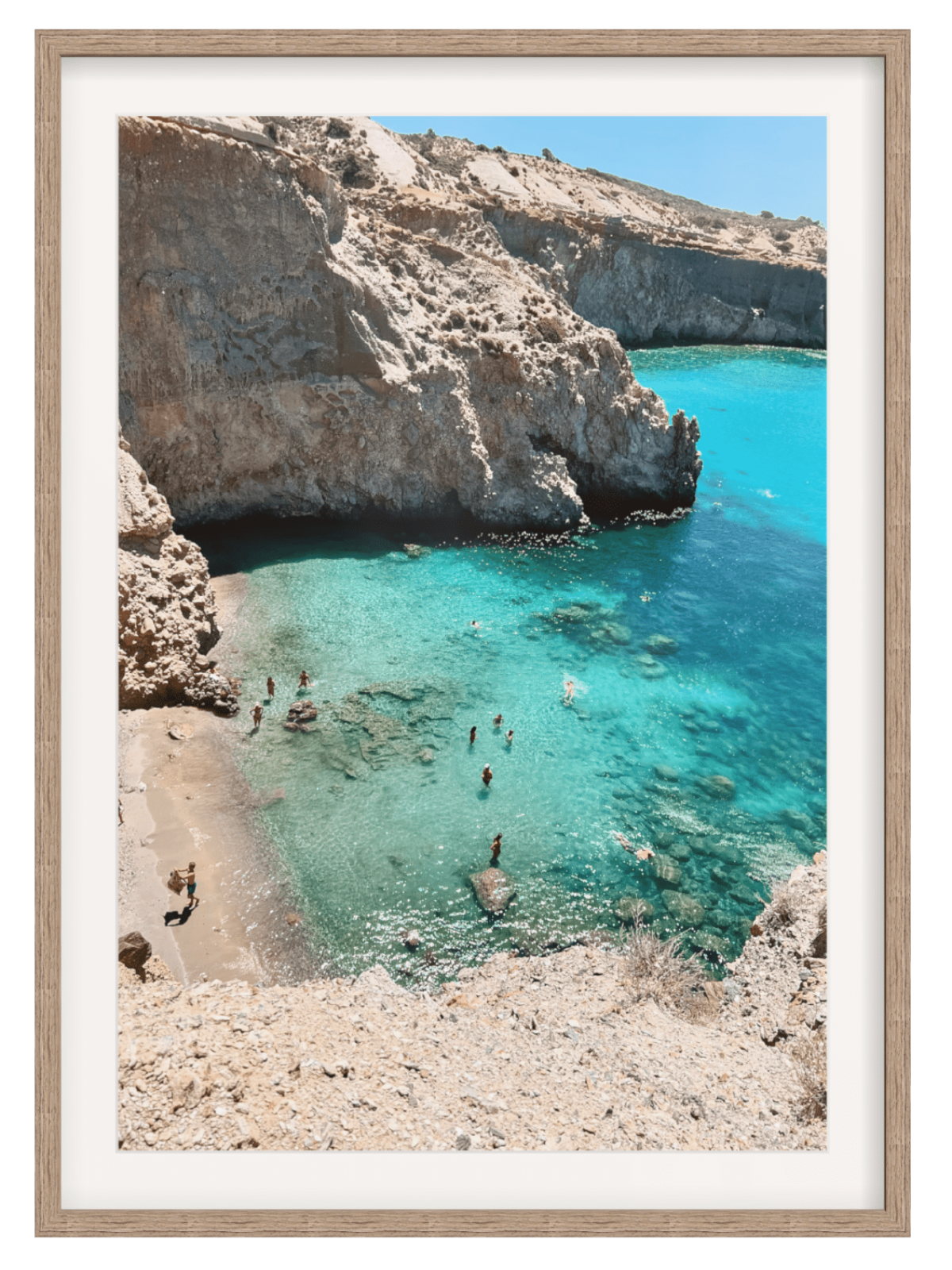 Framed photograph of a rocky beach with clear blue water and people swimming.