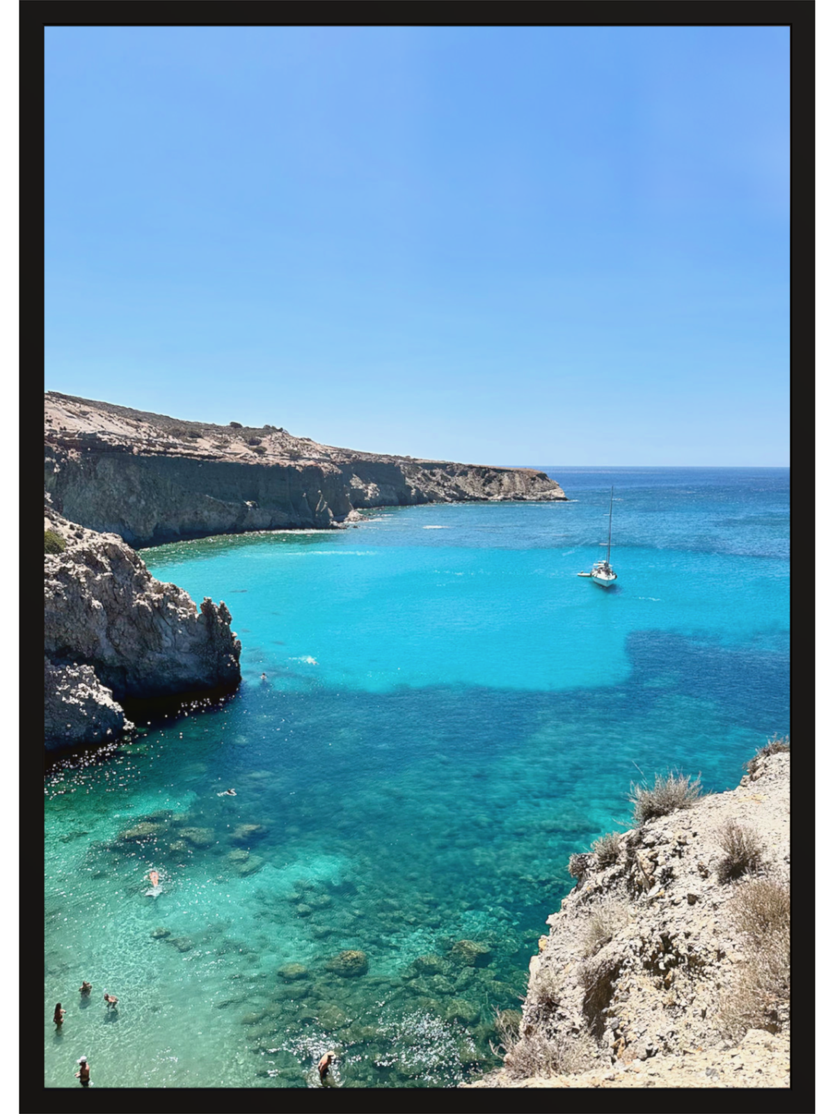 Turquoise sea with a boat and people near cliffs under a clear blue sky.