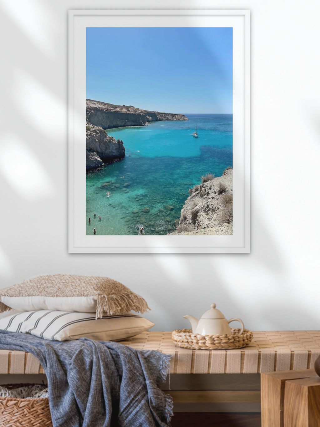 Framed photograph of a coastal scene with clear blue water and cliffs, displayed on a wall above a wooden table.