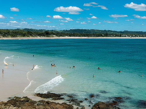 Beach scene with clear blue water and people swimming, under a partly cloudy sky.
