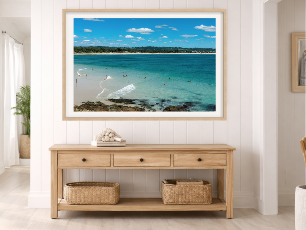 Framed beach scene print on a wall above a wooden console table with baskets.