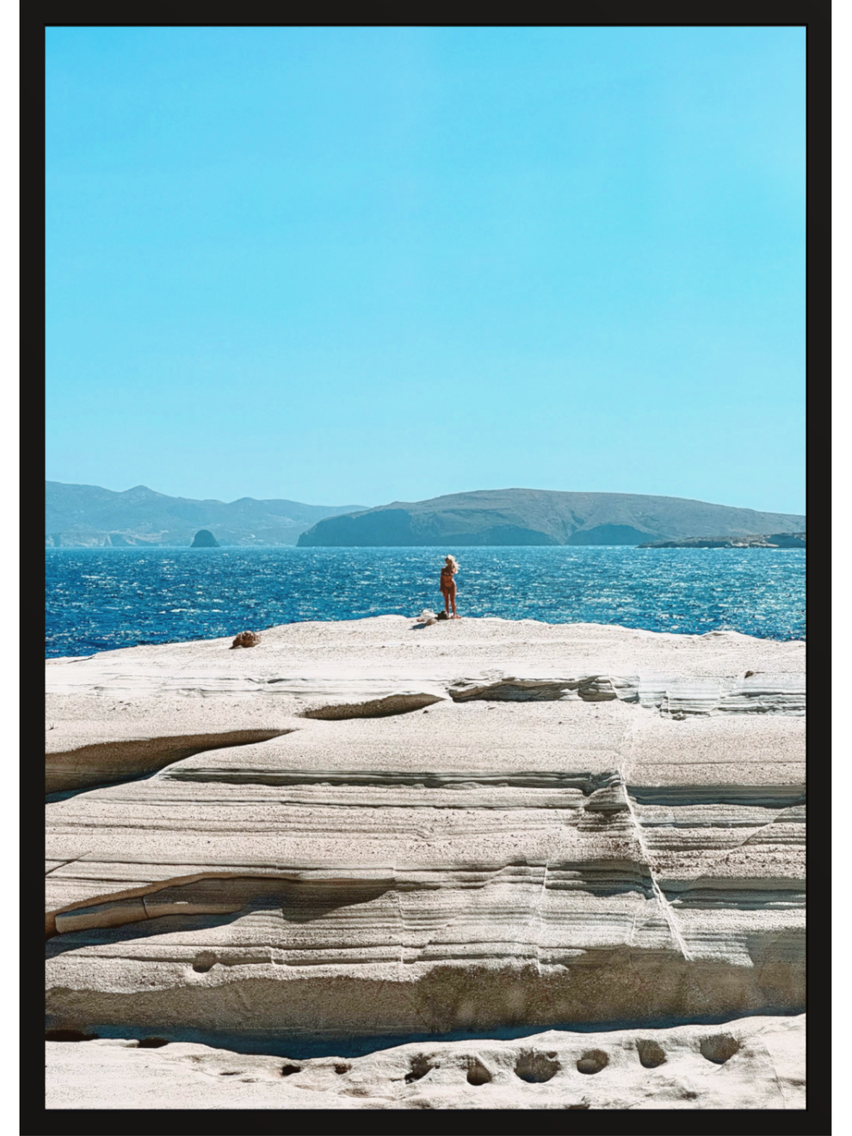 Person standing on a rocky outcrop overlooking the ocean with islands in the distance.