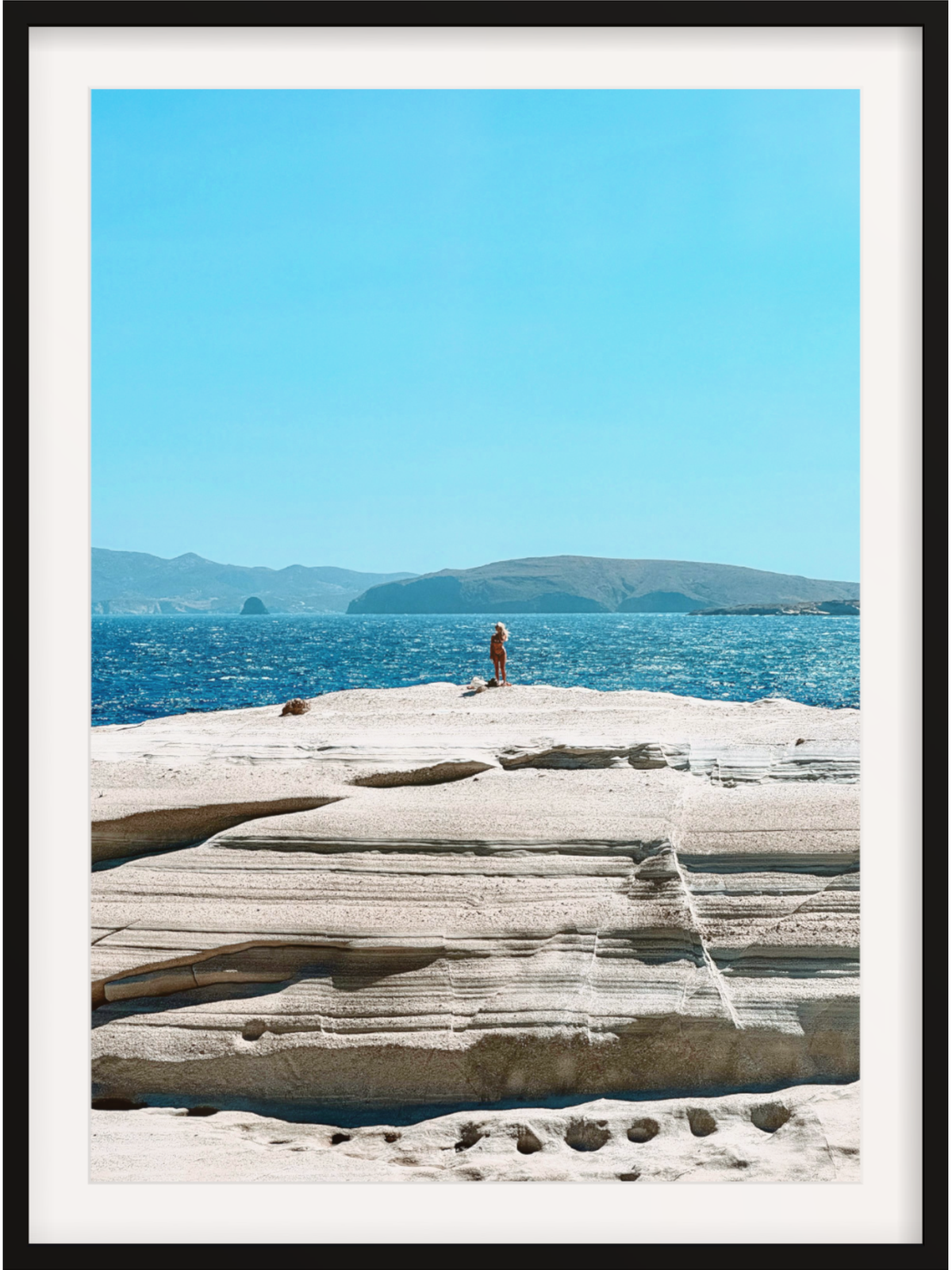 Person standing on a rocky outcrop by the ocean with mountains in the background