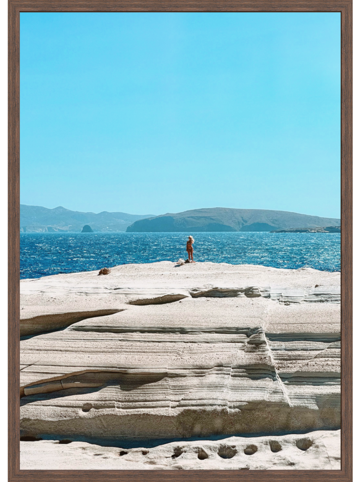 Person standing on a rocky outcrop by the ocean with clear blue sky