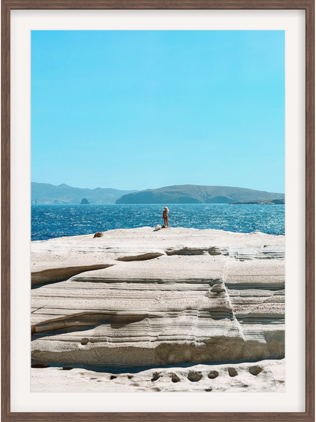 Person standing on a rocky outcrop with blue water and sky in the background