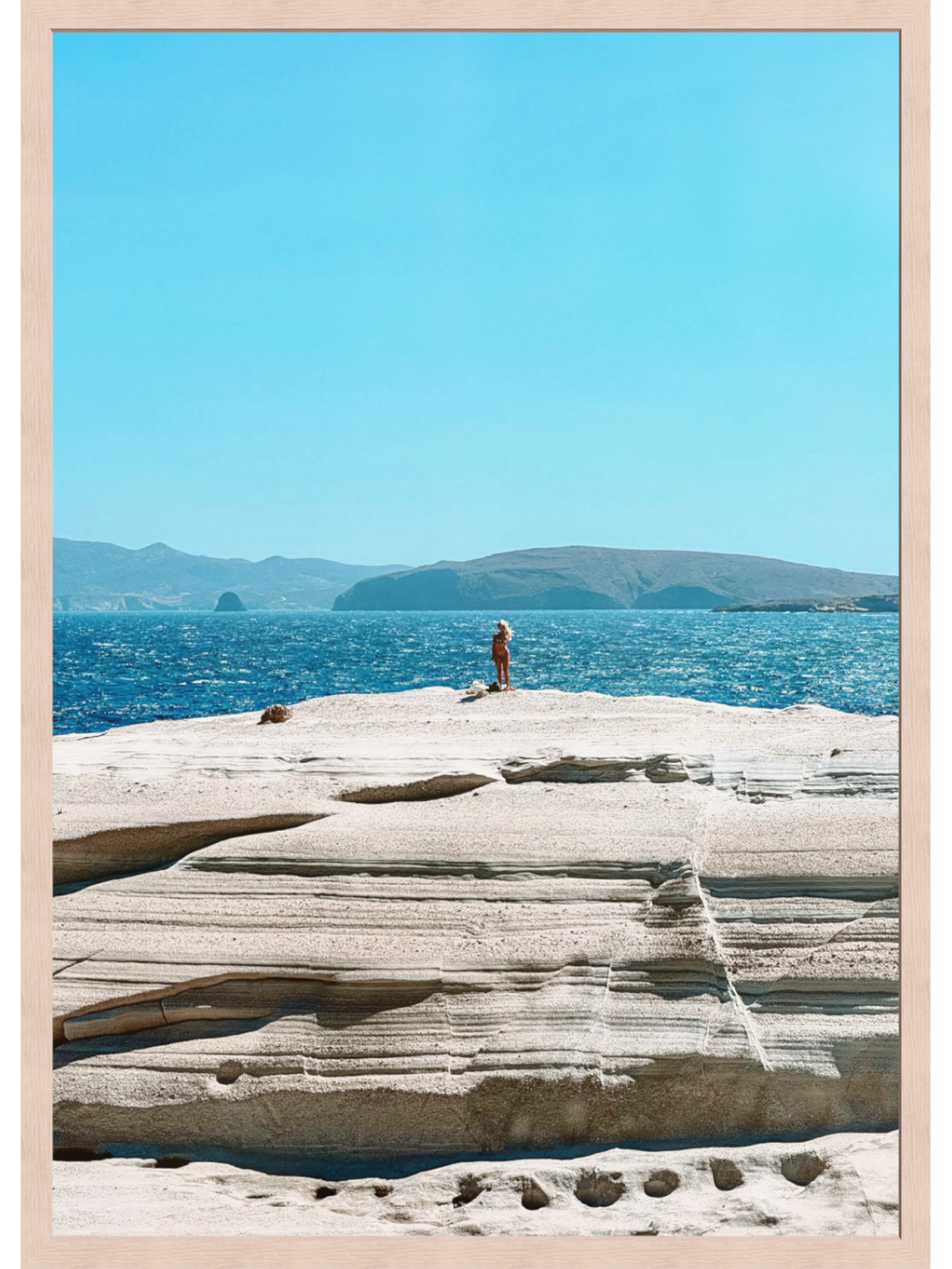 Person standing on a rocky outcrop overlooking the ocean with mountains in the background.