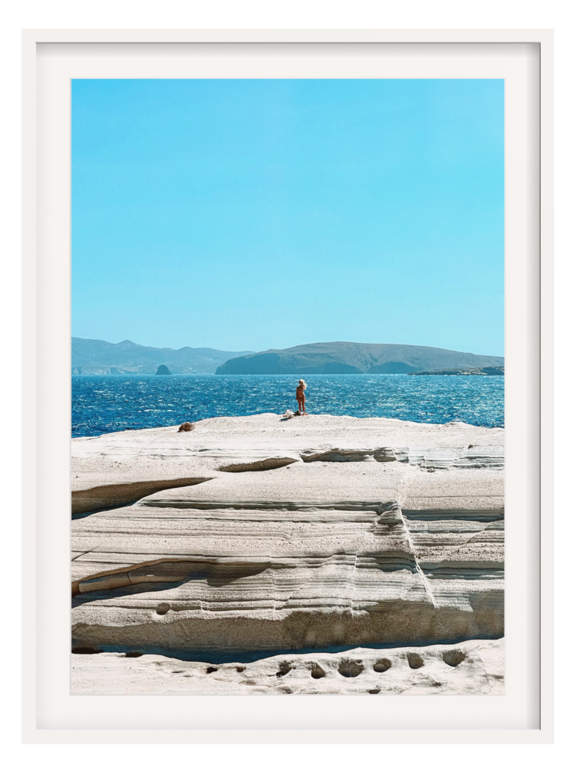 Person standing on a rocky outcrop with blue water and sky in the background