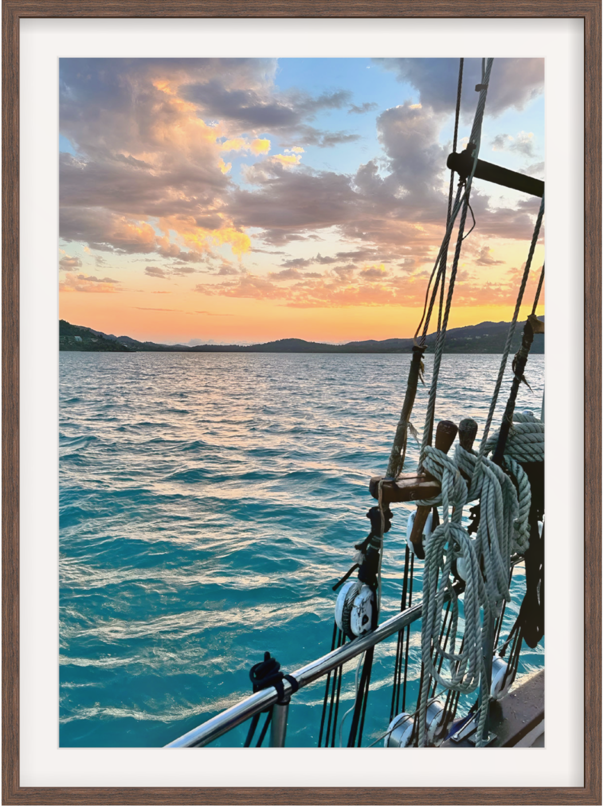 Framed photograph of a sunset over the ocean with a sailboat's rigging.