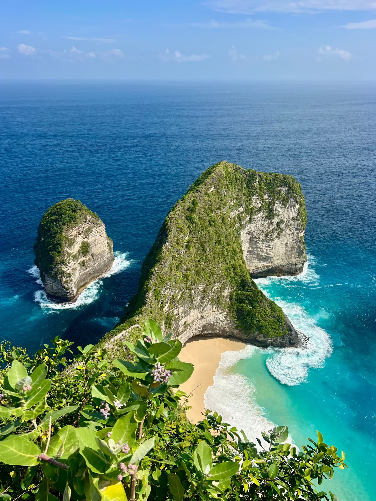 Two large rock formations with a sandy beach surrounded by clear blue water.