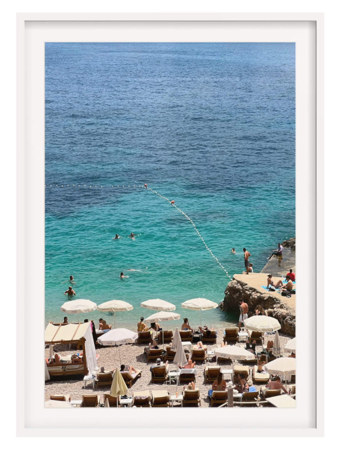 Beach scene with people, umbrellas, and lounge chairs near a cliff overlooking the ocean.white frame with border