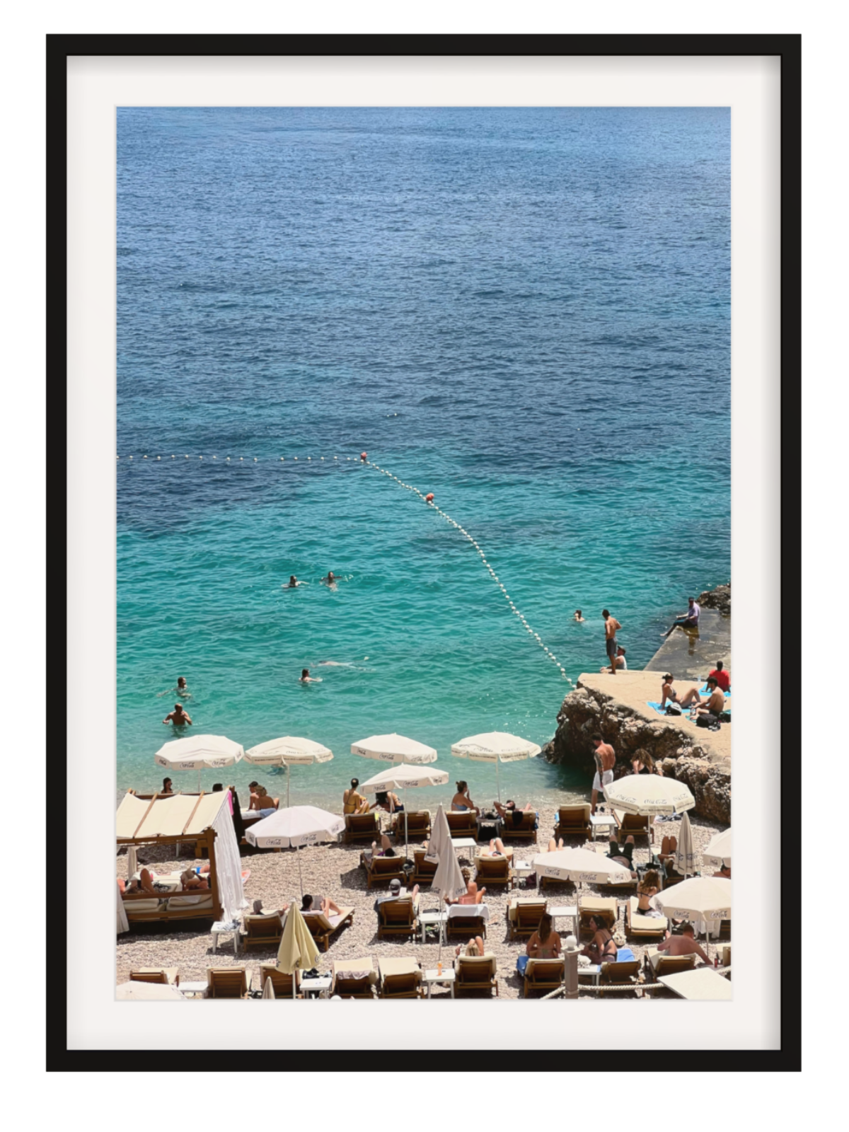 Beach scene with people, umbrellas, and lounge chairs near a body of water. black frame with border