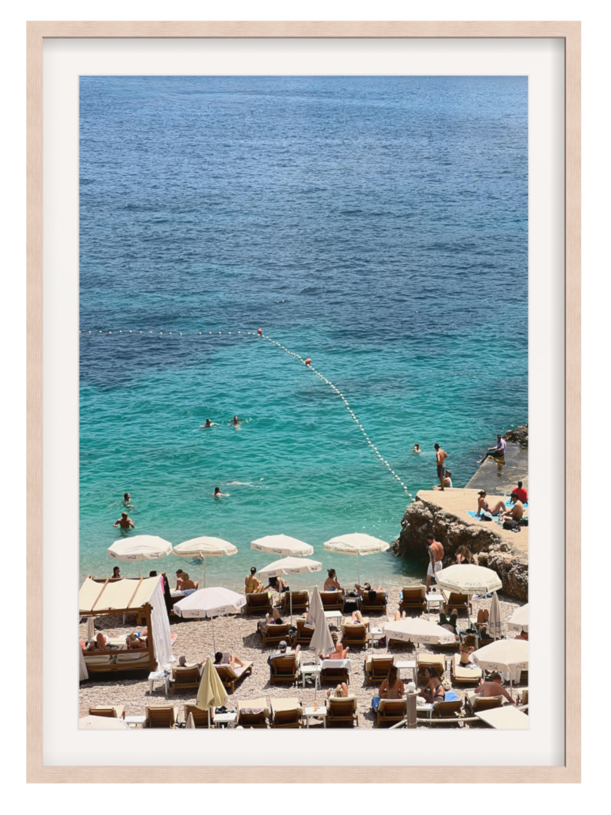 Beach scene with people, umbrellas, and lounge chairs near a cliff overlooking the ocean. light oak frame with border