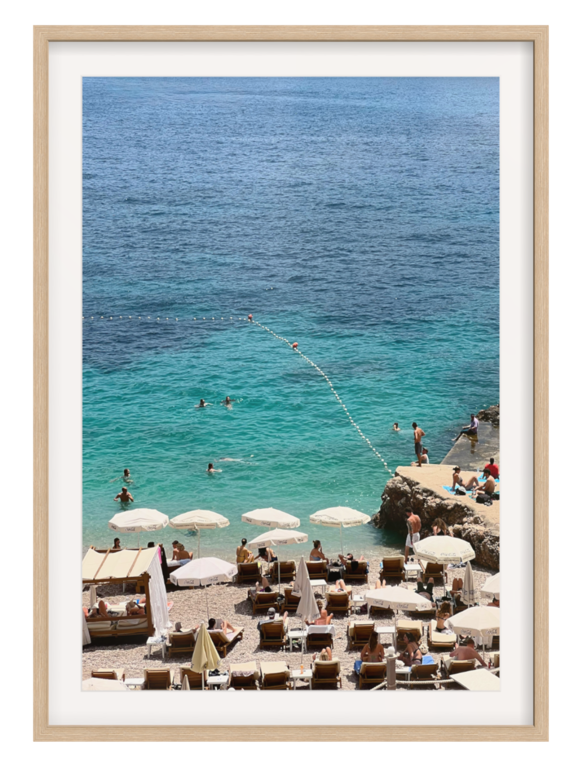 Framed photograph of a beach scene with people, umbrellas, and clear blue water.