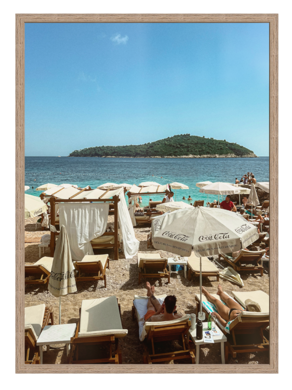 Beach scene with people, umbrellas, and chairs under a clear blue sky.