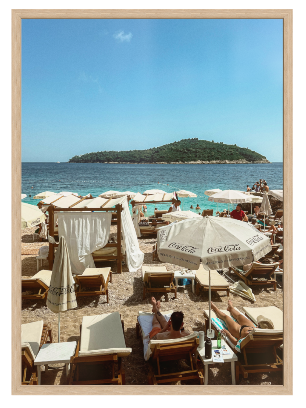 Beach scene with people under Coca-Cola umbrellas and a distant island.