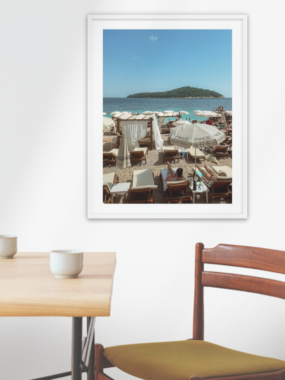 Framed photograph of a beach scene above a dining table with chairs.