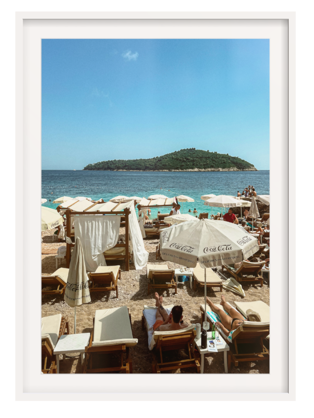 Beachside cafe with Coca-Cola umbrellas and lounge chairs, overlooking a small island.