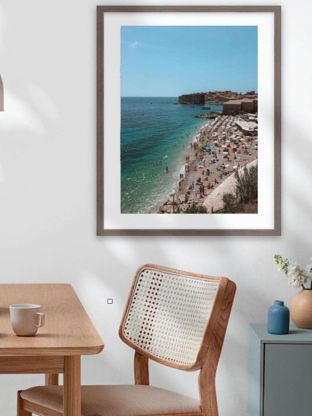 Framed photograph of a coastal scene above a dining table with a bowl of fruit.