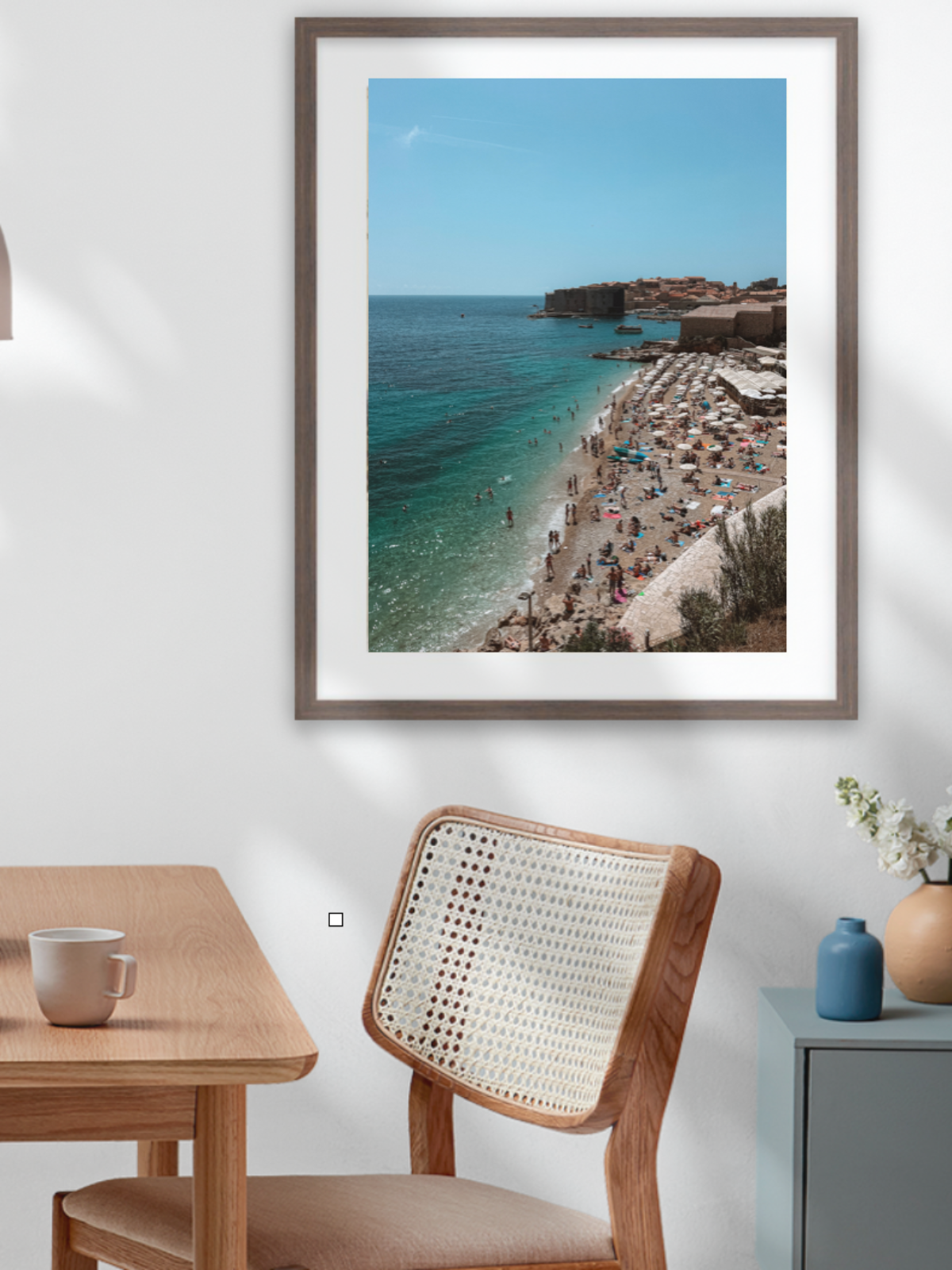 Framed photograph of a coastal scene above a dining table with a bowl of fruit.
