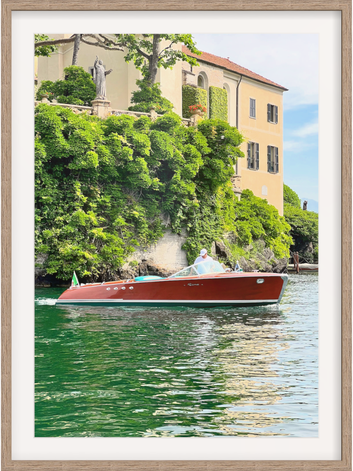 Red boat on a canal with a building and trees in the background, framed in a wooden manner.