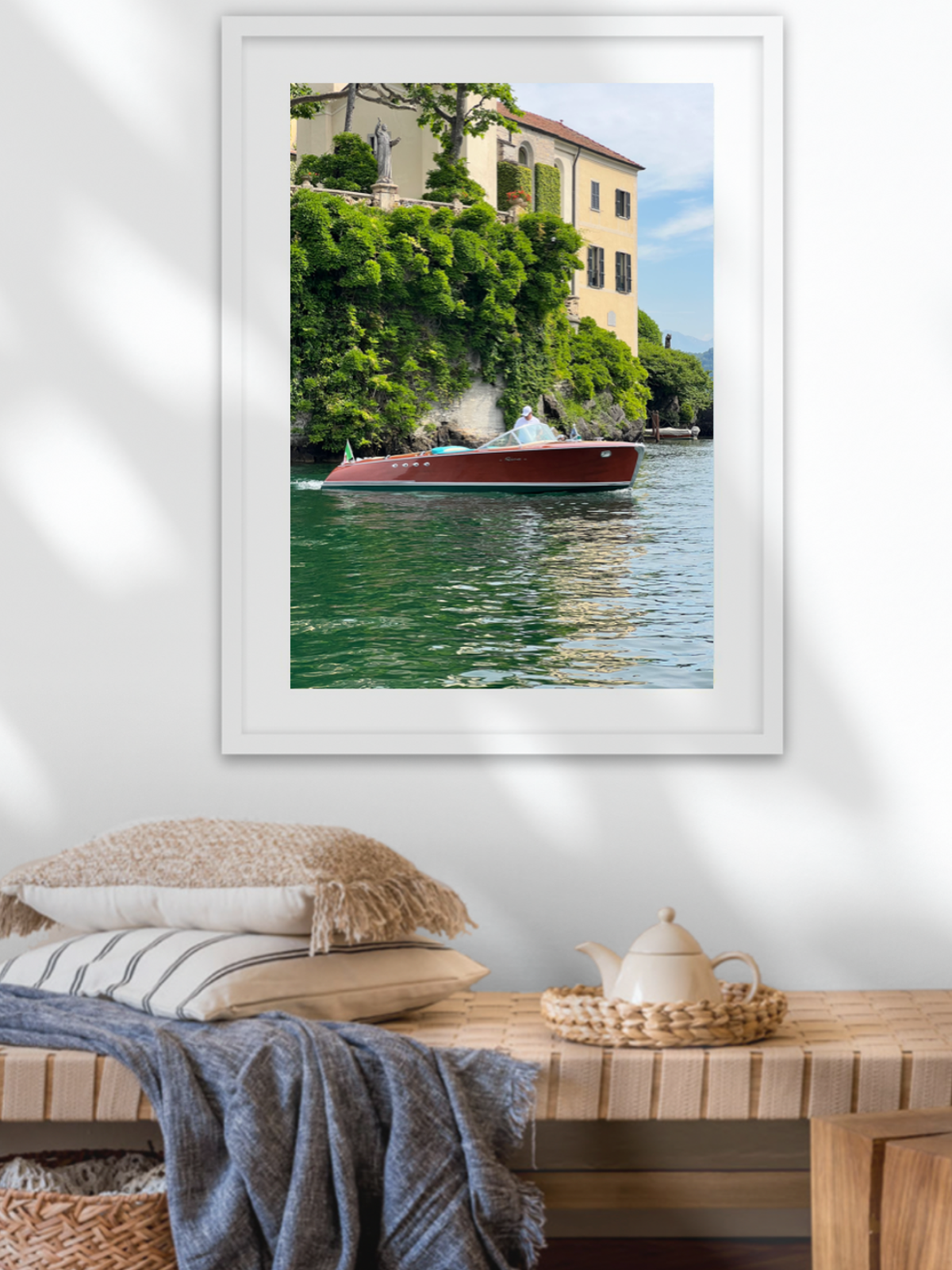 Framed photograph of a boat on a canal with greenery and buildings in the background, displayed above a wooden bench.